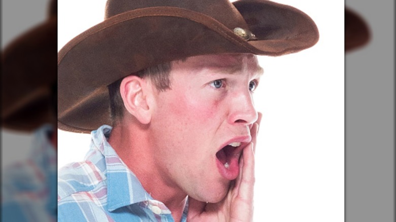cowboy holding his cheek in discomfort and yelling