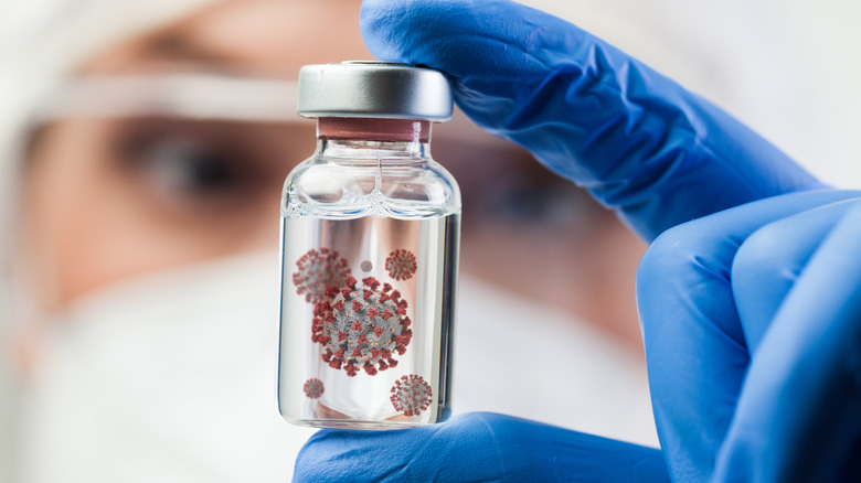 Masked researcher holding up a vial with a blue gloved hand examining a COVID-19 mutation