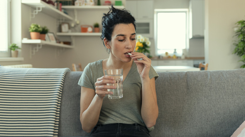 woman taking a supplement while sitting on a couch