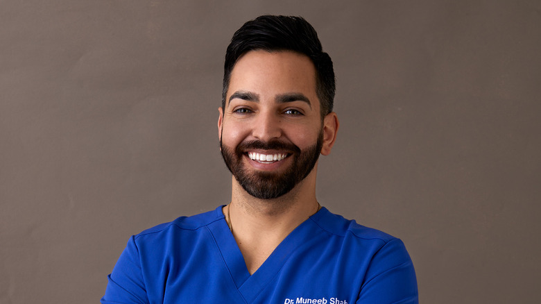 Dr. Muneeb Shah in blue scrubs, smiling