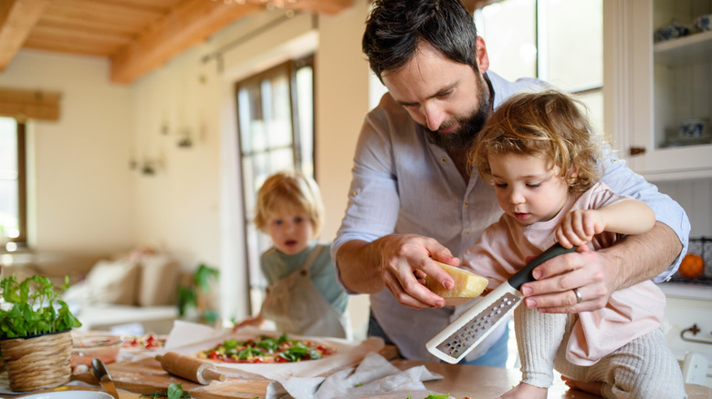 man grating cheese in kitchen with little children