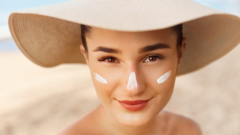 Woman wearing hat, with sunscreen on face, at beach