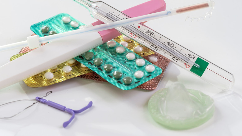 Birth control pills, an IUD, a condom, a pregnancy test, a thermometer, and an ovulation test on a white table