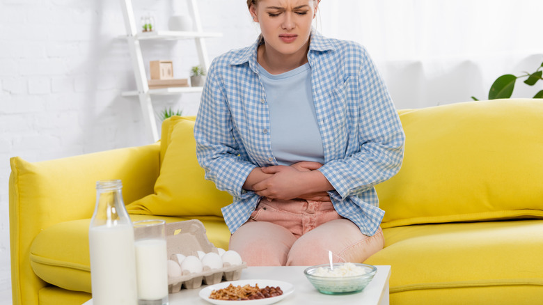 woman holding her painful stomach while sitting in front of dairy products