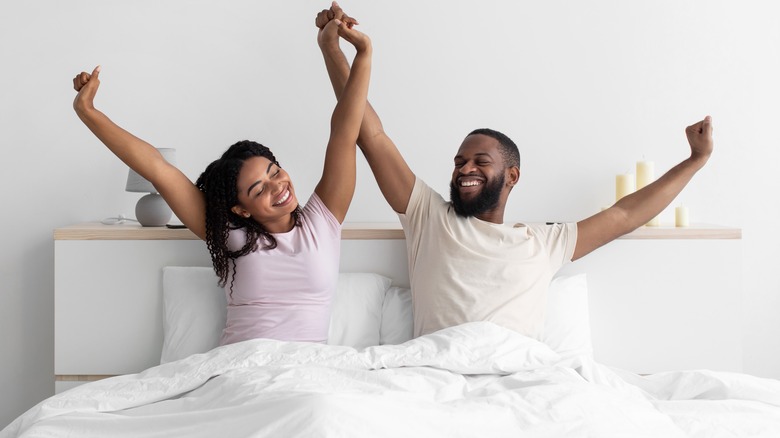 Man and woman waking up and stretching happily in bed while holding hands