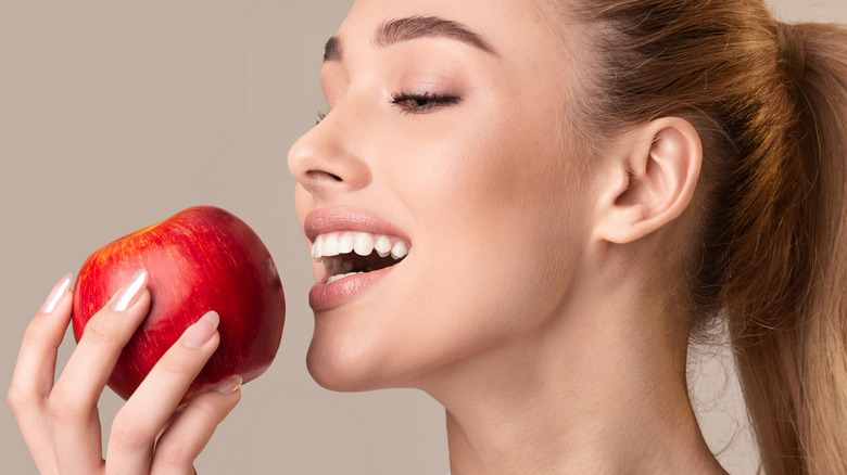 Woman smiling with an open mouth about to bite down on a red apple