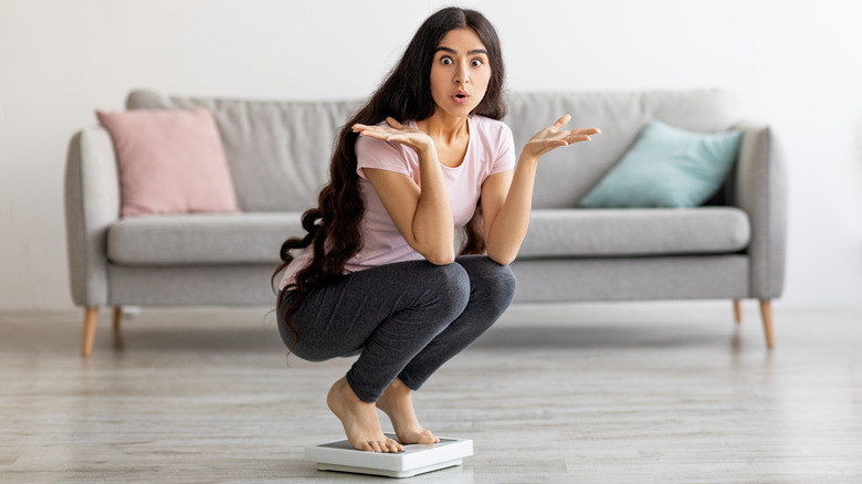 woman squatting while on a scale, questioning its accuracy