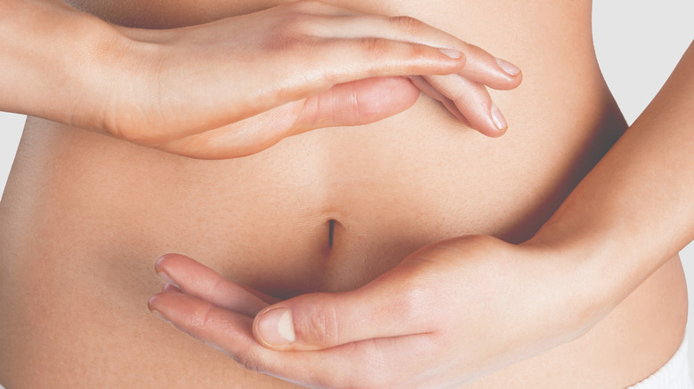 a woman uses her hands to depict balance in the gut, close up of tummy 