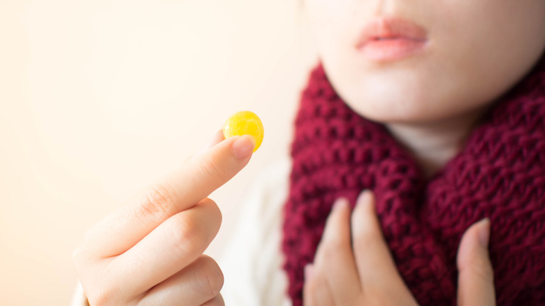 A woman with a cold takes a cough drop