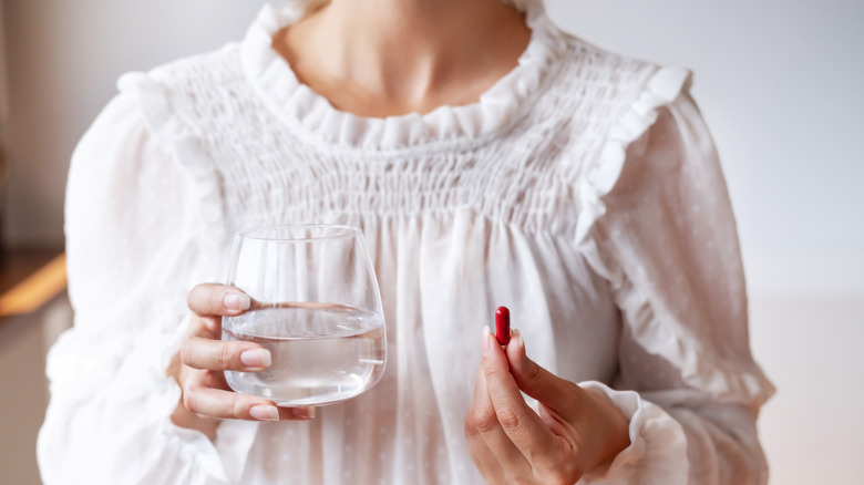 Woman holding glass of water and supplement 