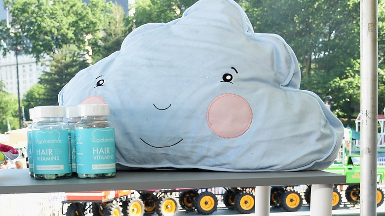 Several bottles of SugarBearHair vitamins next to a cloud pillow