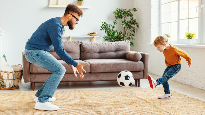 Adult and child playing soccer in a living room