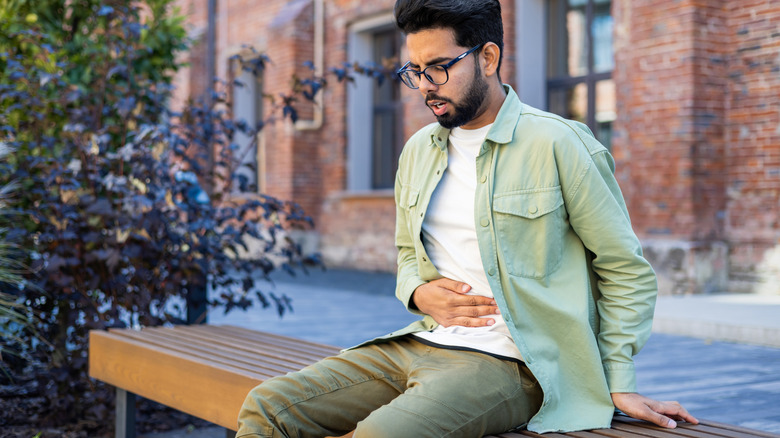 young man holding sick stomach outside on bench