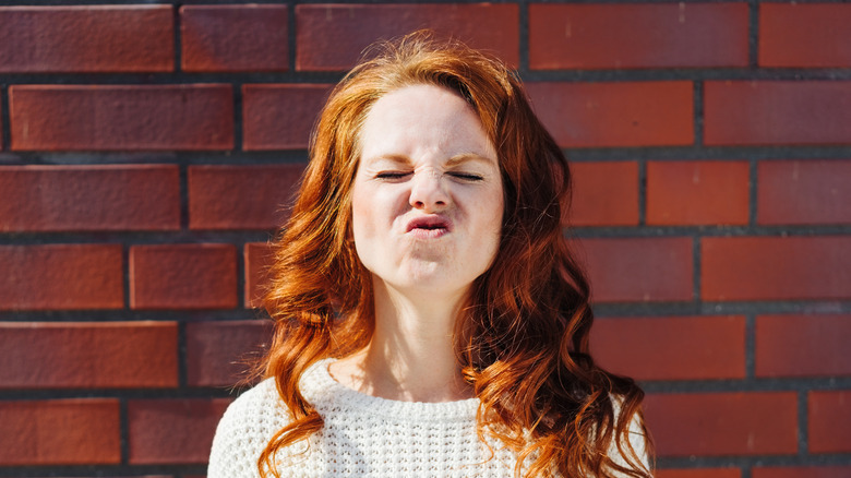brick wall behind woman crinkling nose 