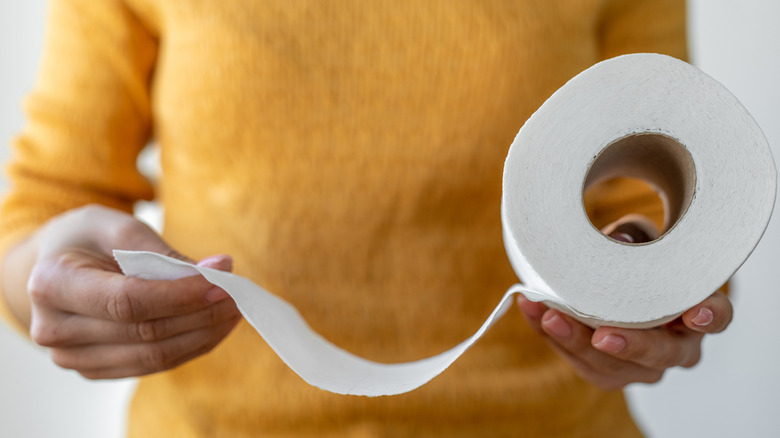A woman holding a roll of toilet paper and pulling out several sheets of it