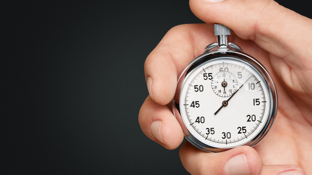 a male hand holding a small silver clock 