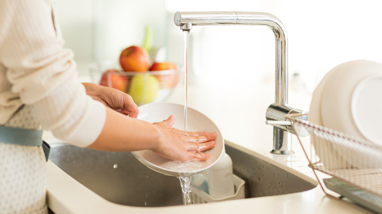 Close up of hand washing a dish in kitchen sink next to drying rack