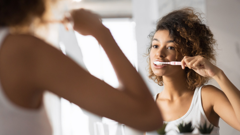 Reflection of woman brushing her teeth in the bathroom mirror