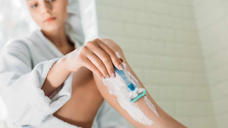 A woman shaves her legs with shaving cream