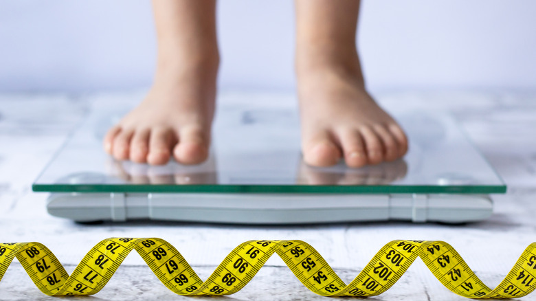 a child's feet on a scale with a measuring tape in front 