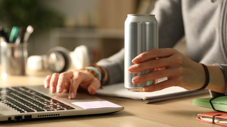 working on computer holding energy drink