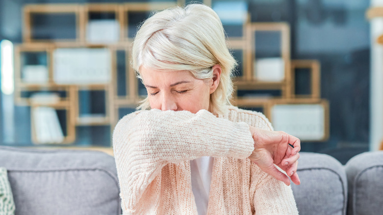 Older woman sneezing into arm