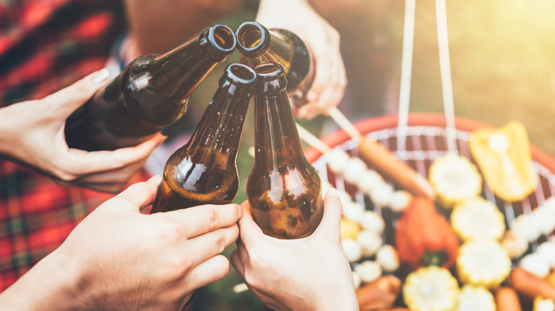 Group of hands cheersing their beer bottles over a grill