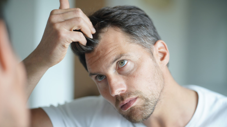 A man looks at his hair in the mirror