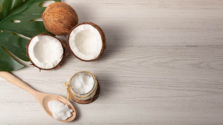 One coconut cracked in half next to a jar of coconut oil