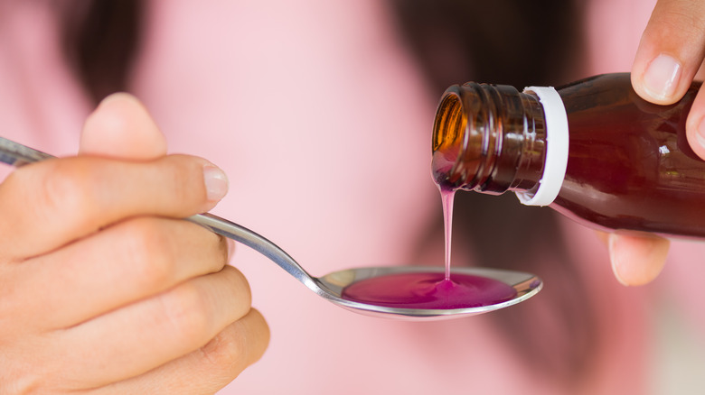 Close up of hands pouring pink liquid cough syrup onto silver spoon