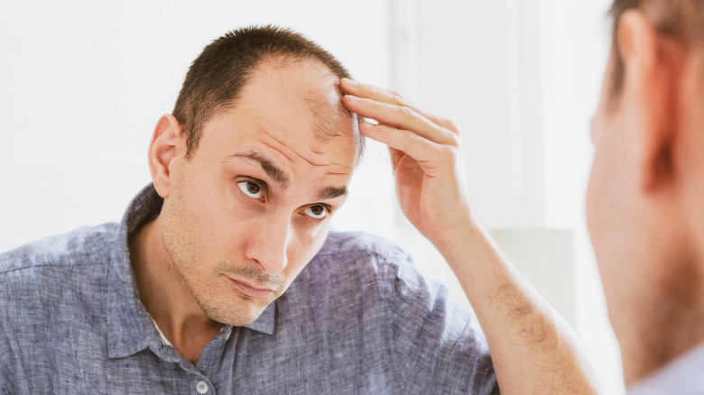 A balding man looks at his hair in the mirror