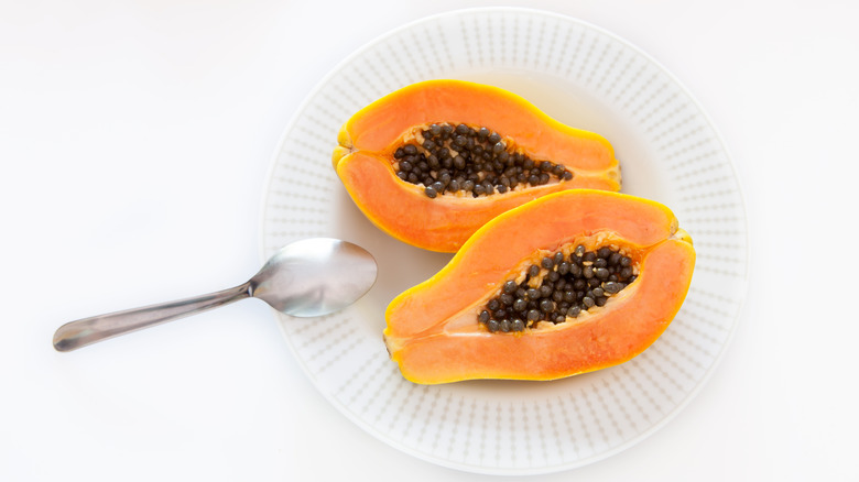 A papaya is cut open on a plate next to a spoon