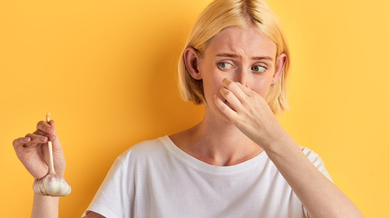 Woman holding garlic and plugging her nose