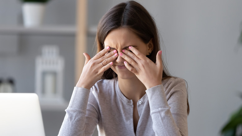 woman holding her head while trying to work on her laptop