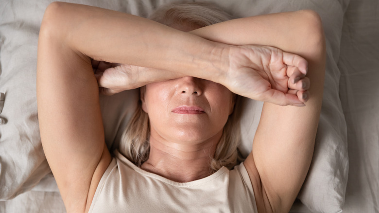 woman in bed with arms covering her head