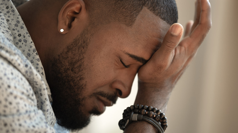 Man grimaces with hand on forehead