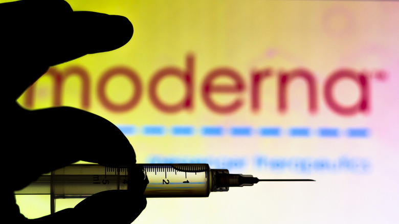 hand holding syringe against a sign reading "Moderna"