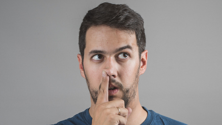 Man on a gray background with finger up his nostril