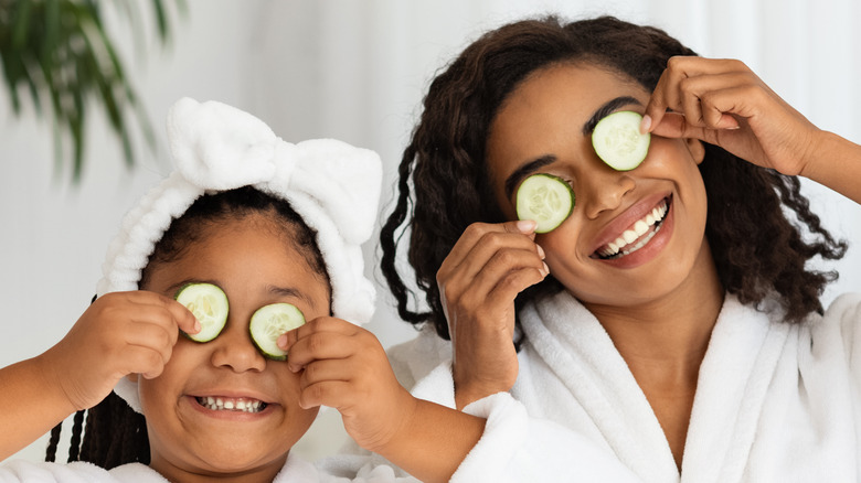 mother and daughter in white robes holding cucumbers to their eyes 