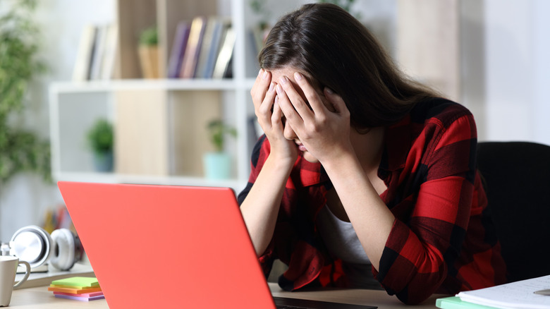 Woman holding face in front of laptop 