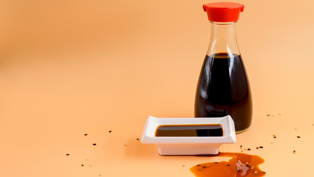 Glass bottle of soy sauce next to a white dipping dish full of soy sauce