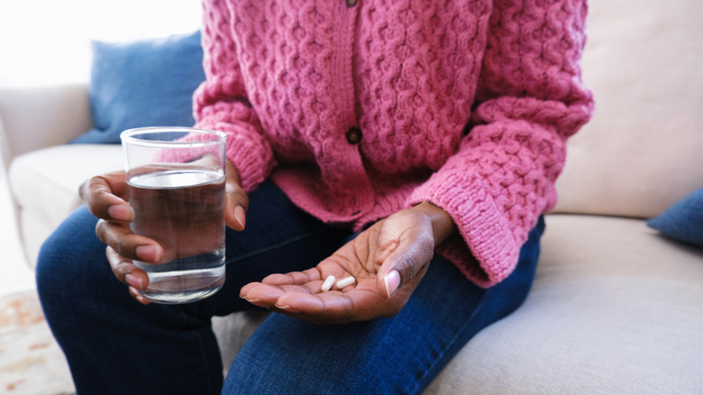 A woman's hands holding pills and a glass of water