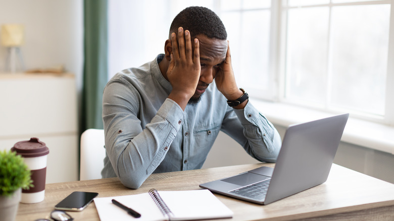 Stressed man at computer, hands at temples