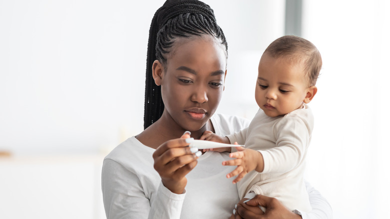 Mother measuring infant's temperature with thermometer