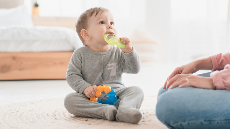Infant gnawing on a toy ring with parent nearby