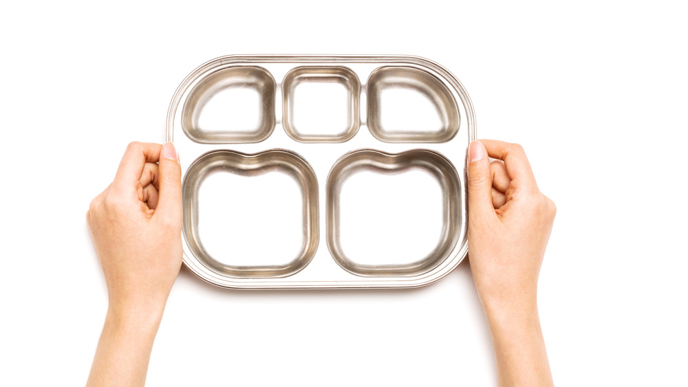 a woman's hands holding a standard rationing food tray with a white background  