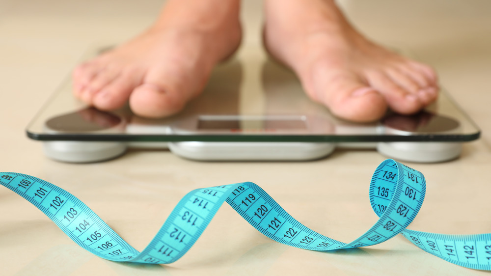 person's feet on the scale with a measuring tape in front 