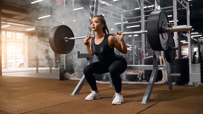 Weightlifter is getting ready to stand with heavy barbell, squatting with weight, looking away with pleasant expression