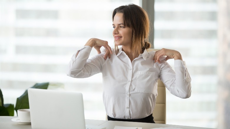 Woman sitting at desk and smiling while doing butterfly wing exercise