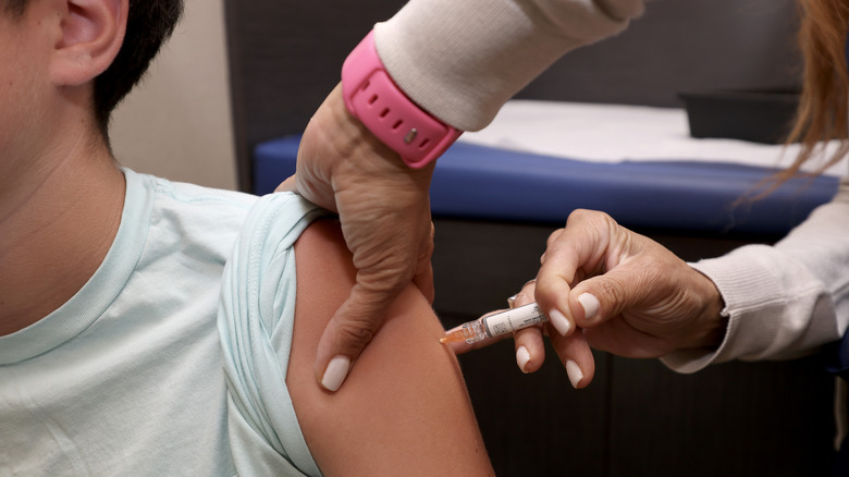 Close up of arm as a woman injects a needle into the arm.